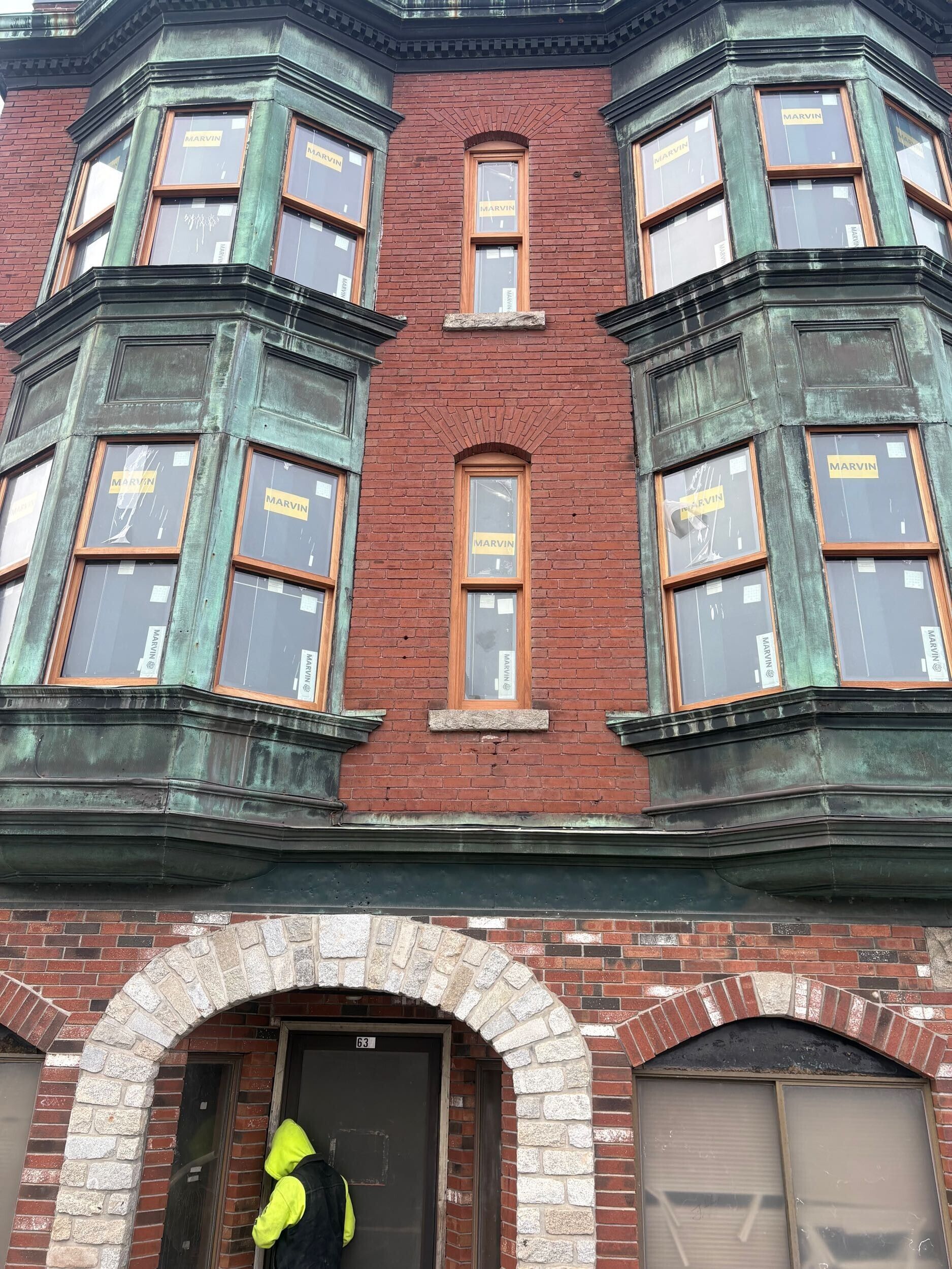 A red brick building with copper-trimmed bay windows and a person in a high-visibility jacket standing at the entrance.