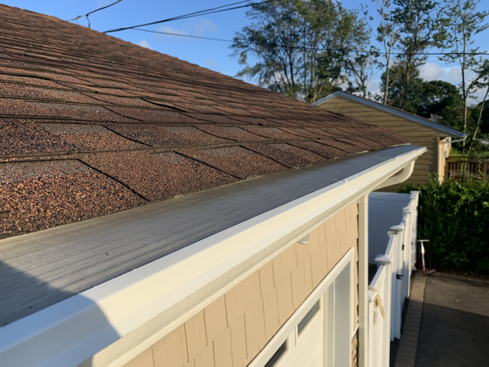 A white gutter is attached to the roof of a house.