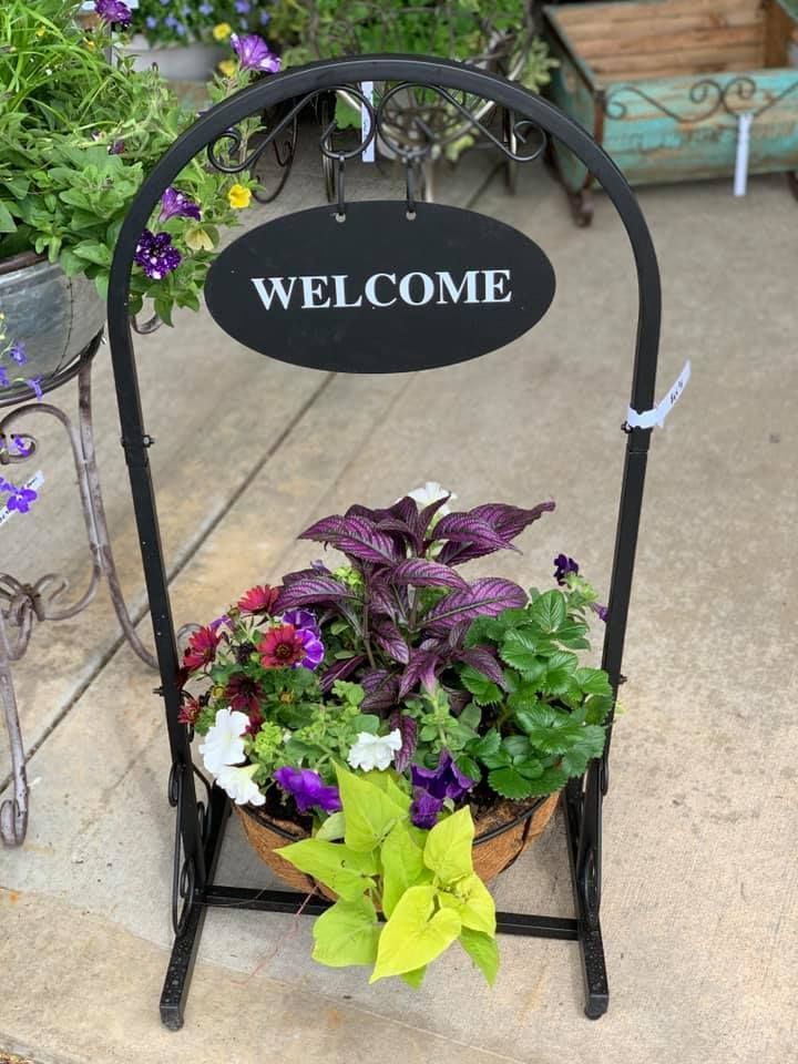 A welcome sign with flowers in a pot on a stand.