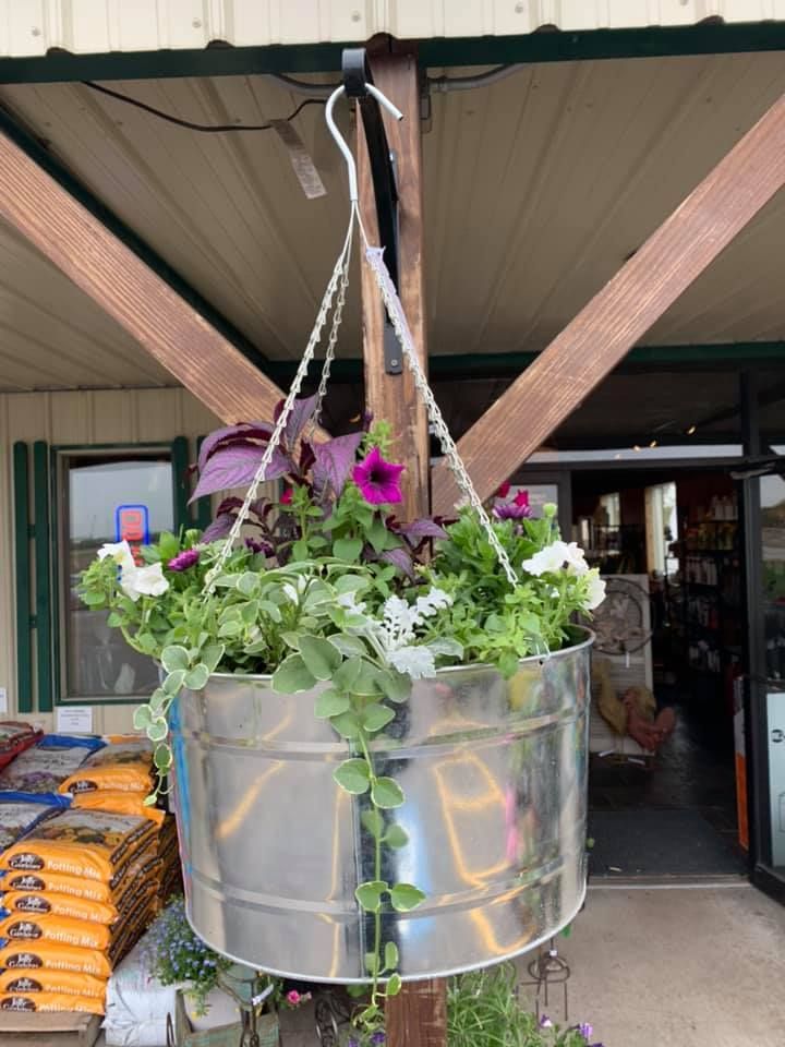 A metal bucket filled with flowers is hanging from a pole.