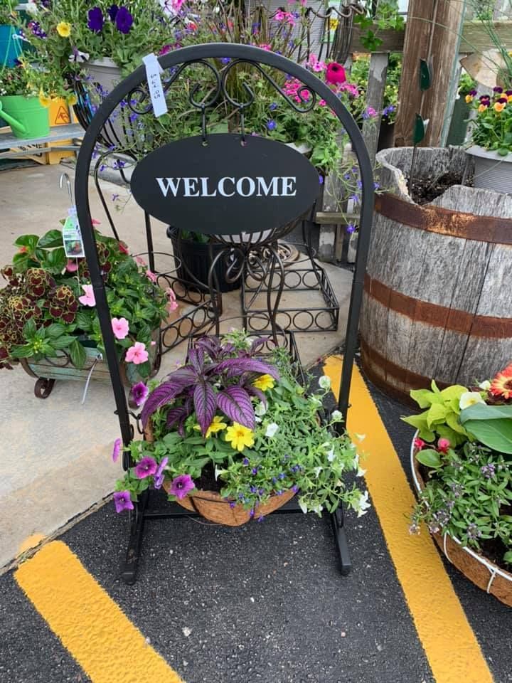 A welcome sign is surrounded by potted plants in a parking lot.
