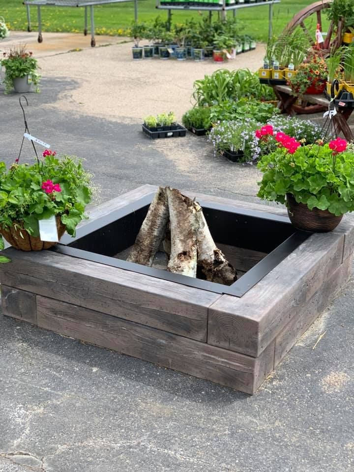 A fire pit with logs in it is surrounded by potted plants and flowers.