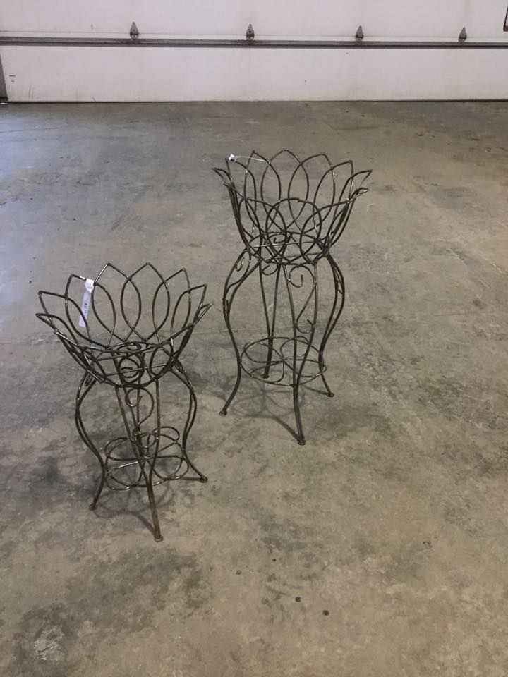 Two wrought iron plant stands are sitting on a concrete floor.