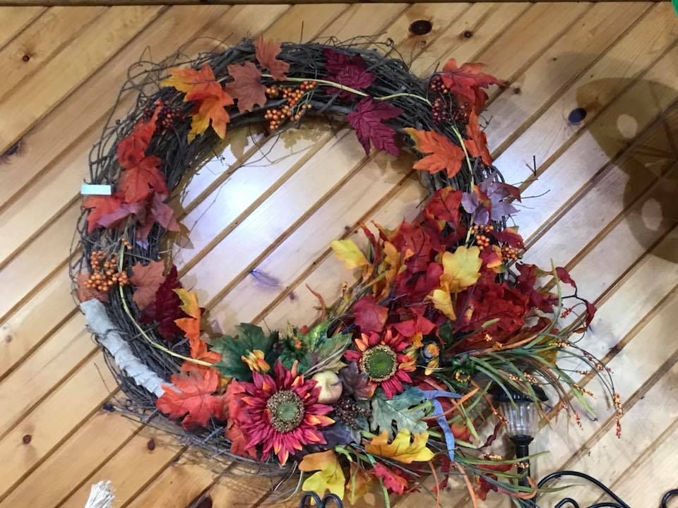 A wreath with leaves and flowers is hanging on a wooden wall.