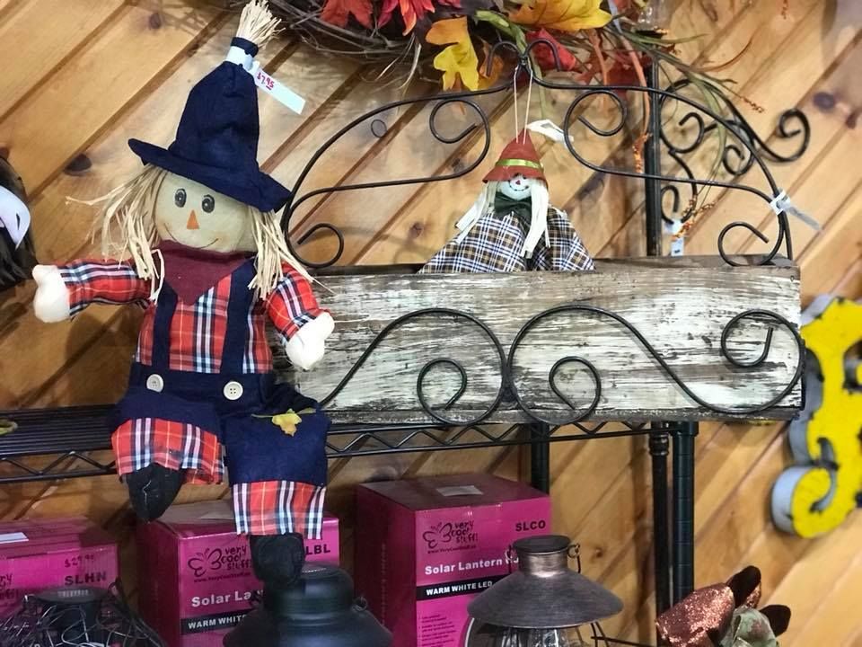 A scarecrow is sitting on a shelf next to a lantern.