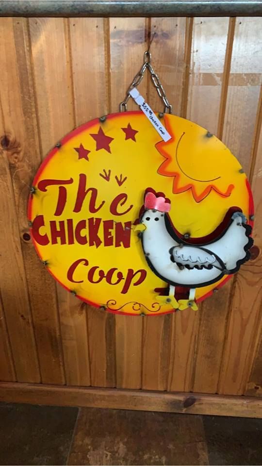 A sign that says `` the chicken coop '' is hanging on a wooden wall.