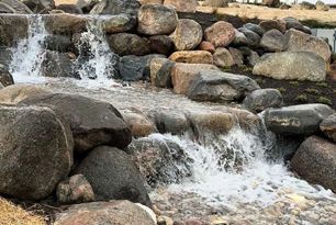 A small waterfall is surrounded by rocks in a park.