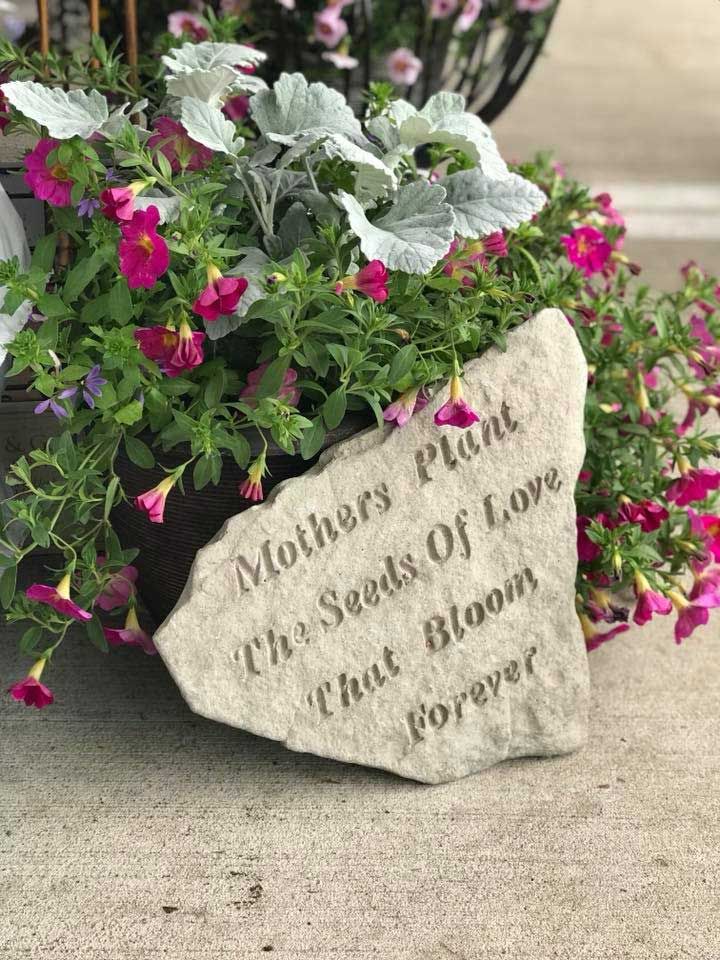 A rock with flowers in it and a quote on it that says `` mothers plant the seeds of love that bloom forever ''.