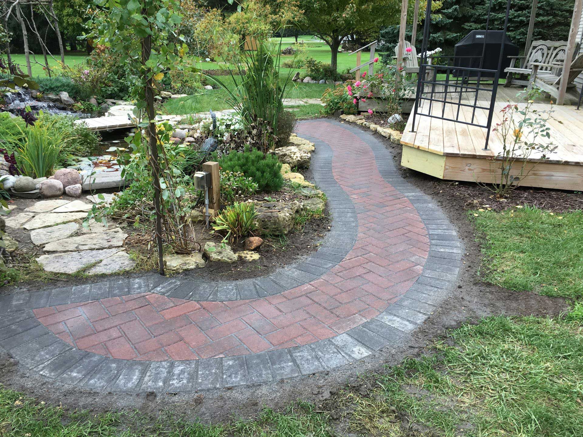 A brick walkway leading to a deck in a garden.