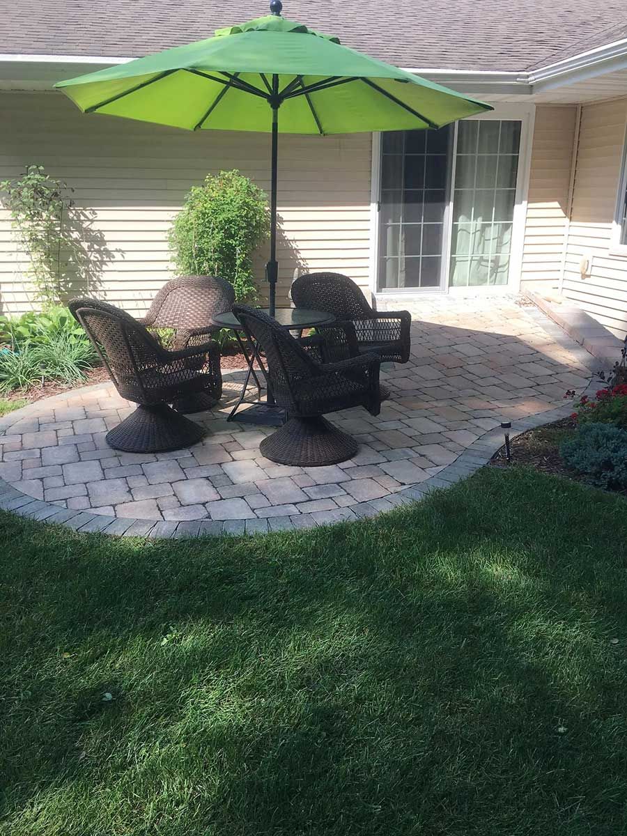 A patio with a table and chairs under an umbrella in front of a house.