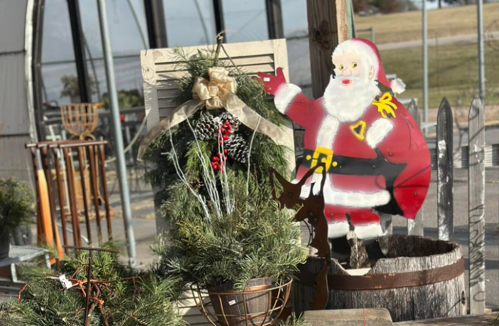 A wheelbarrow filled with flowers, a watering can, boots, and gardening tools.