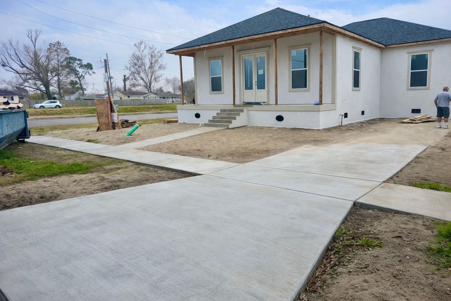 New house under construction with concrete walkway and grass. Man standing near house.