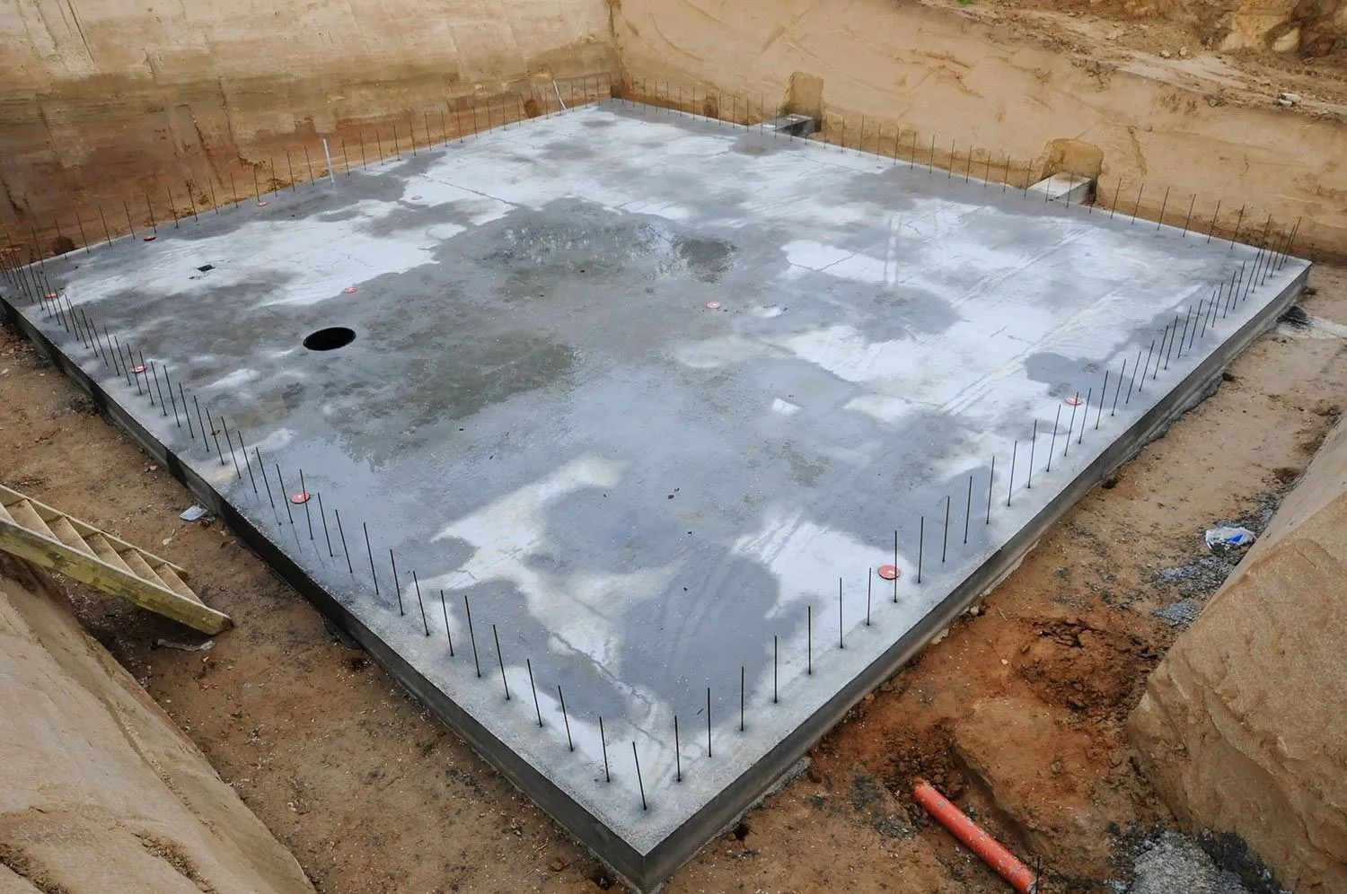 Concrete foundation slab in an earthen excavation. Steel rods project upward.
