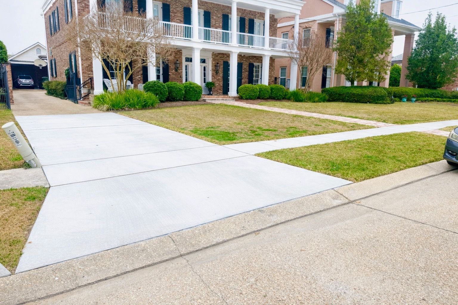 A house with a large concrete driveway and patchy grass.