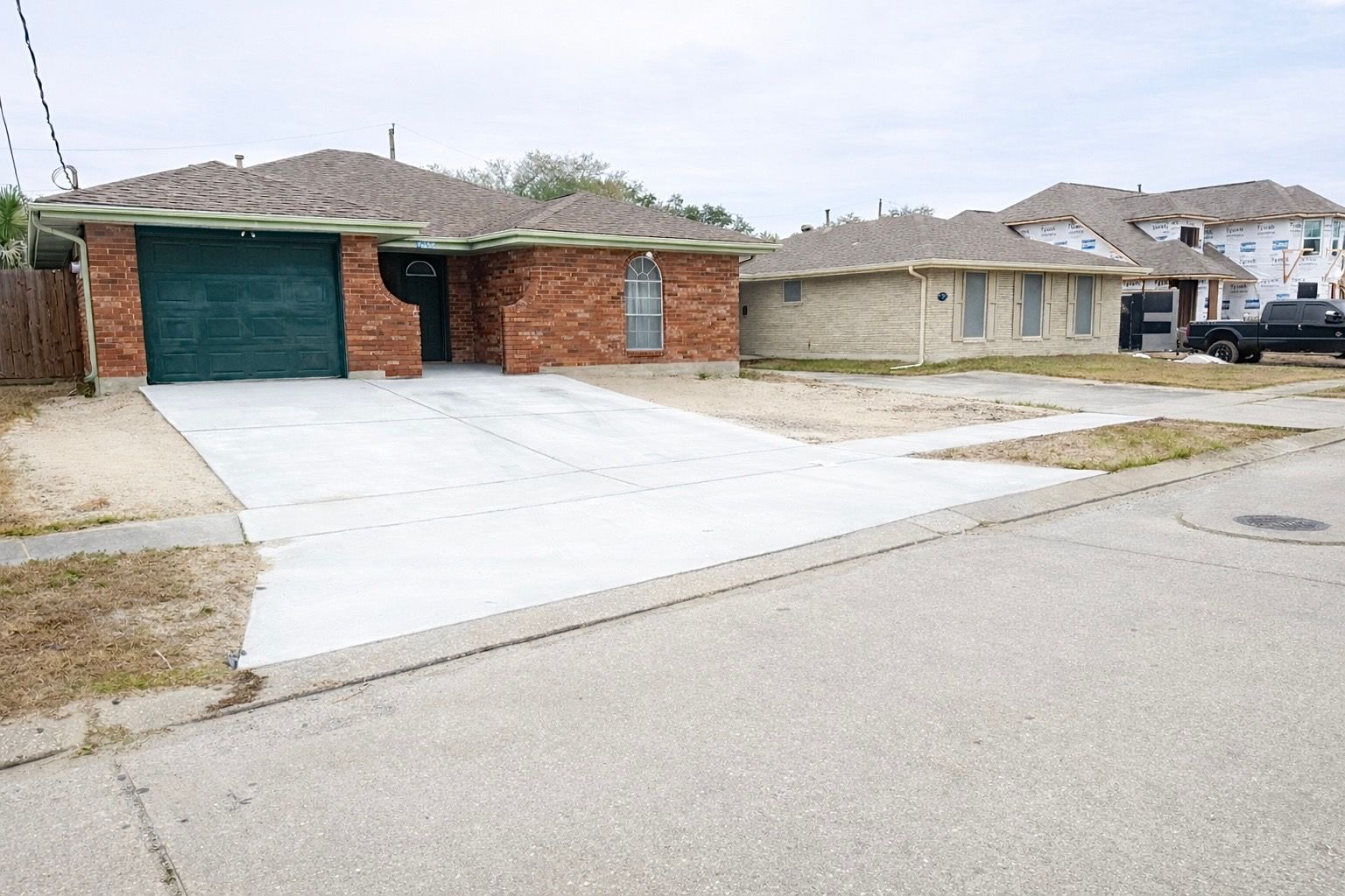 Brick house with green garage door, concrete driveway, and neighboring houses.