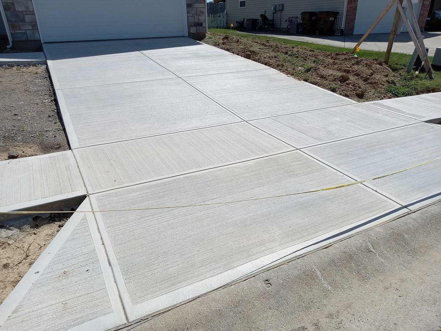 Concrete driveway and sidewalk with grid pattern, in front of a house.