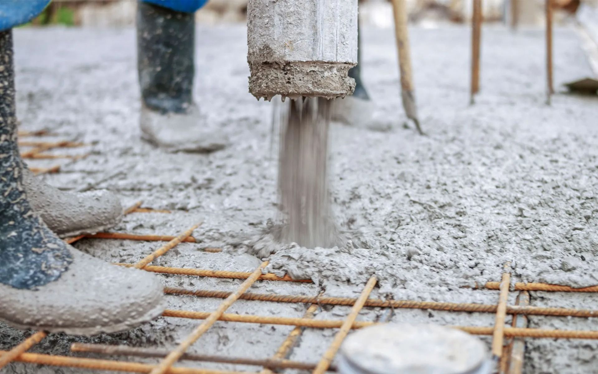 Pouring concrete onto rebar grid, workers' boots visible.