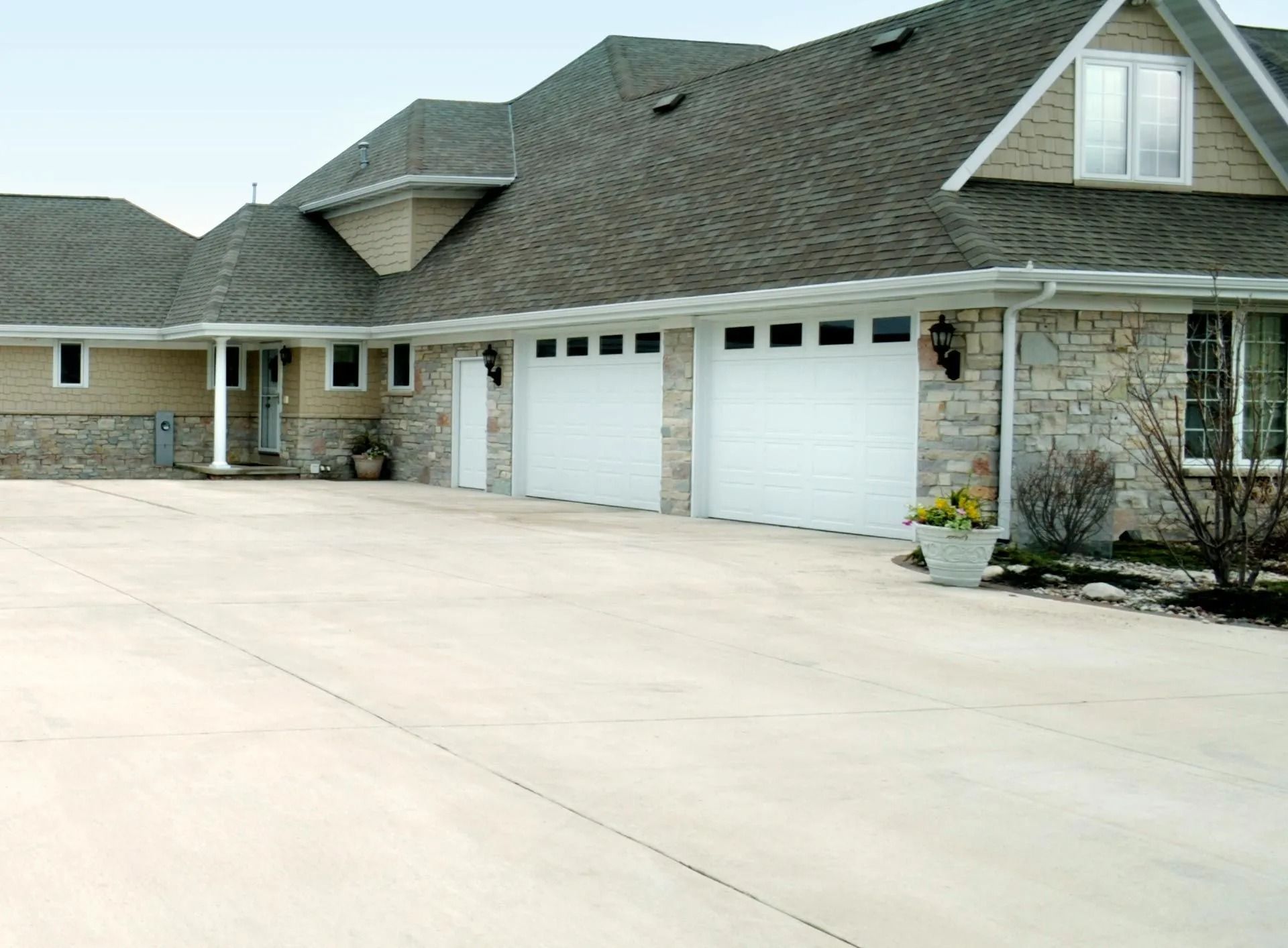 Large beige house with three-car garage and large concrete driveway. Gray roof and stone accents.