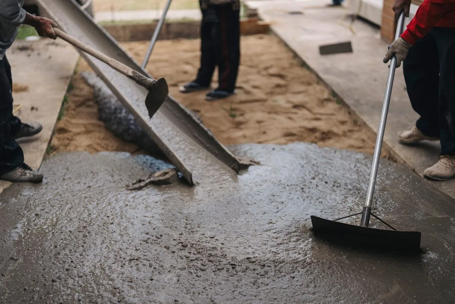 Workers pouring concrete with a chute and smoothing it with a squeegee.