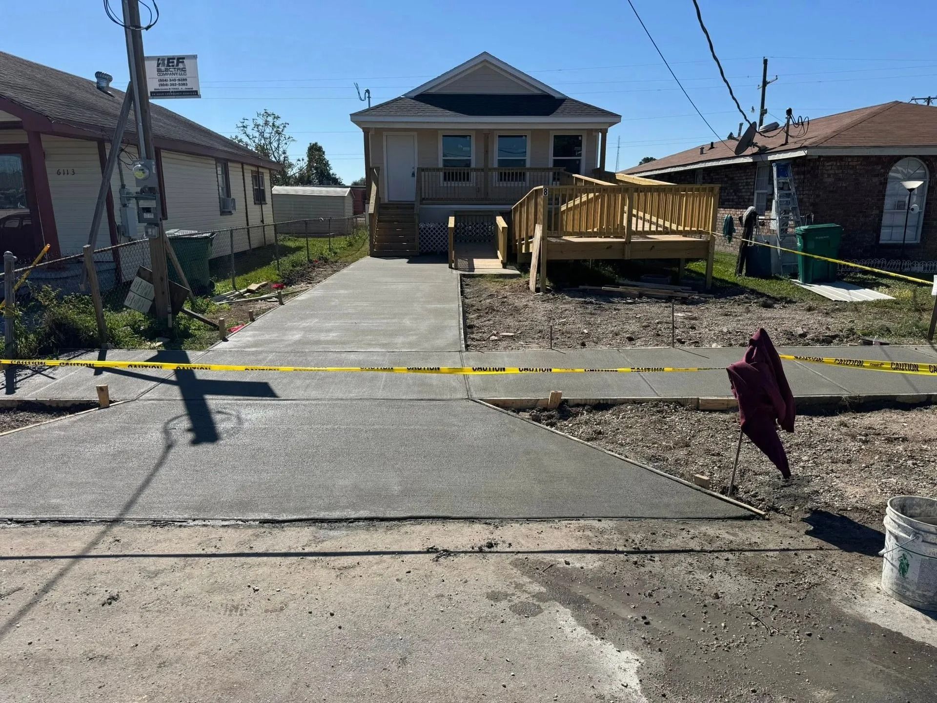 New concrete driveway and walkway leading to a house with a wooden deck; caution tape present.