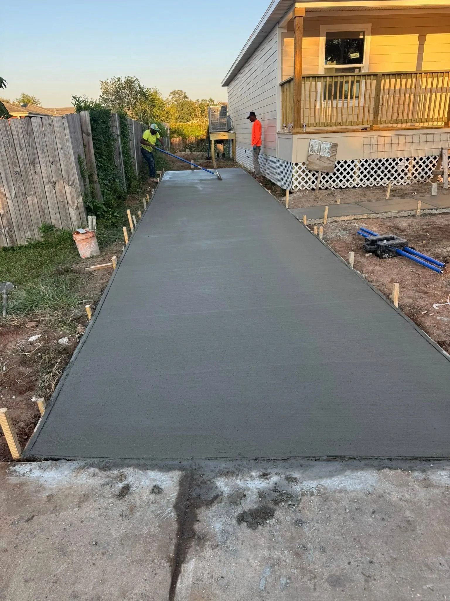 Newly poured concrete driveway with wooden frame, near house under construction.