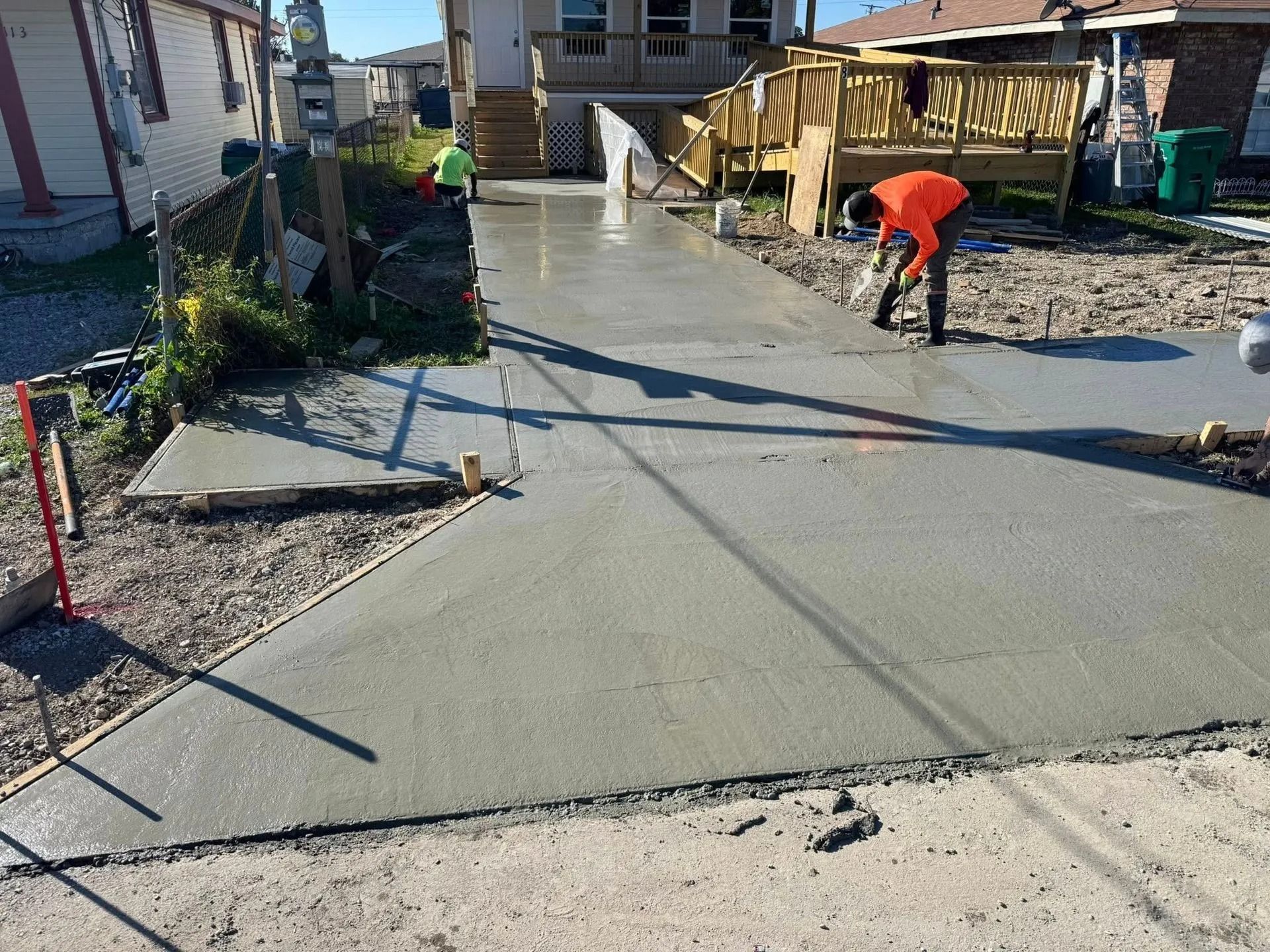 Workers finishing a newly poured concrete driveway and sidewalk.