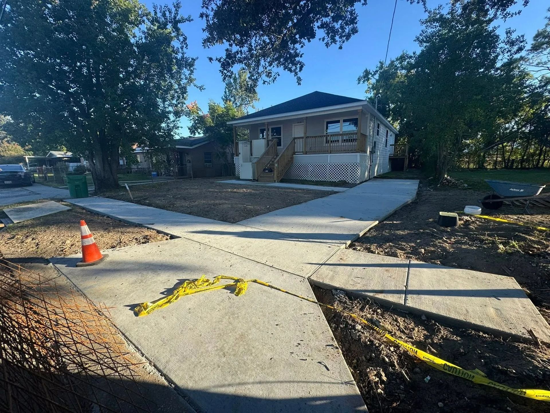 New concrete sidewalks cross in front of a house. Orange cone and caution tape are present.