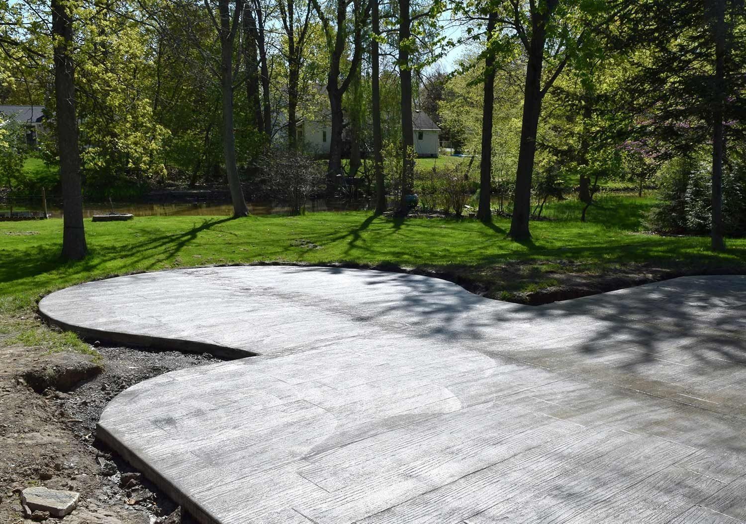 Newly poured concrete driveway curves into a grassy yard with trees in the background.