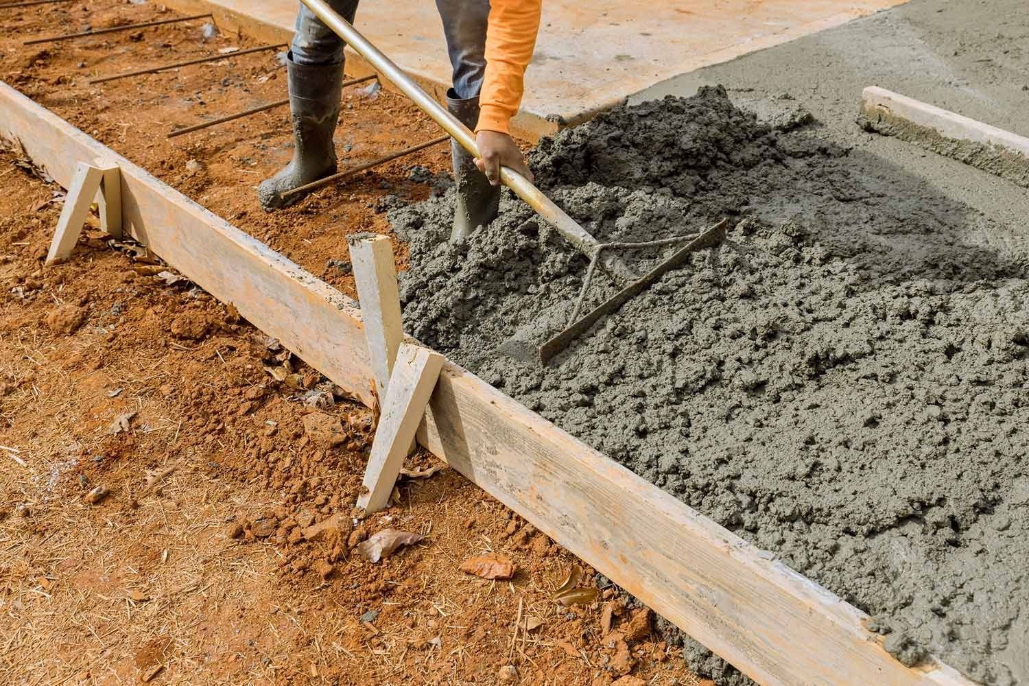 Person rakes wet concrete within wooden forms; rebar in background.