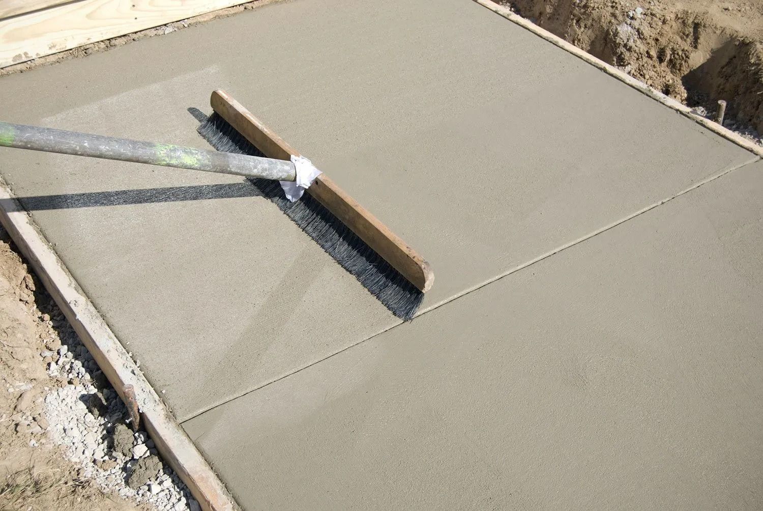 Fresh concrete being leveled with a screed in a wooden form.