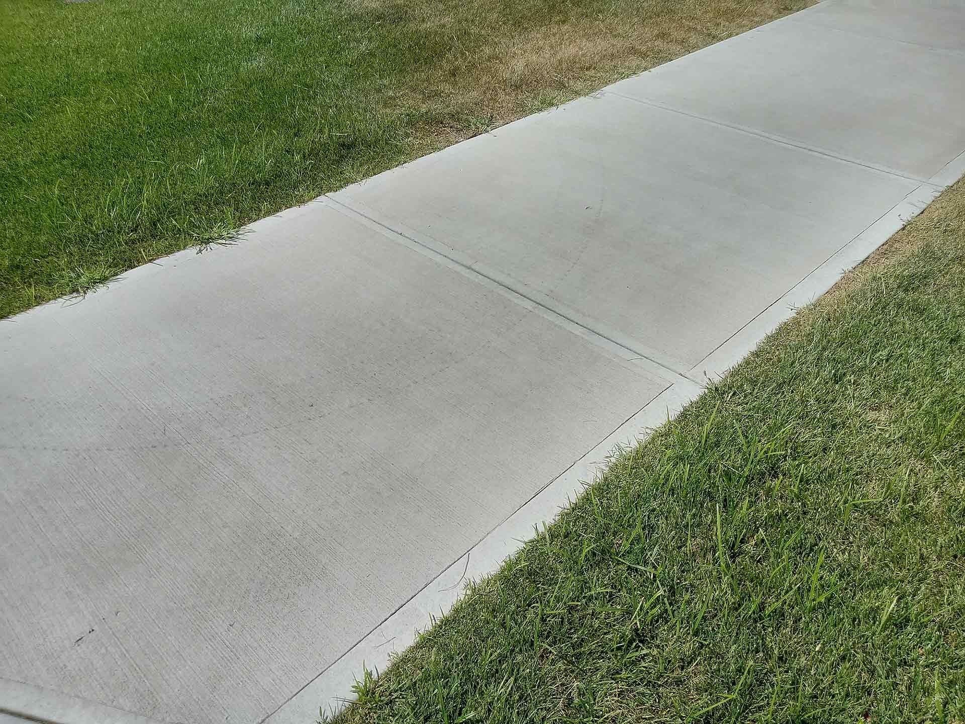 Concrete sidewalk bordered by green grass.