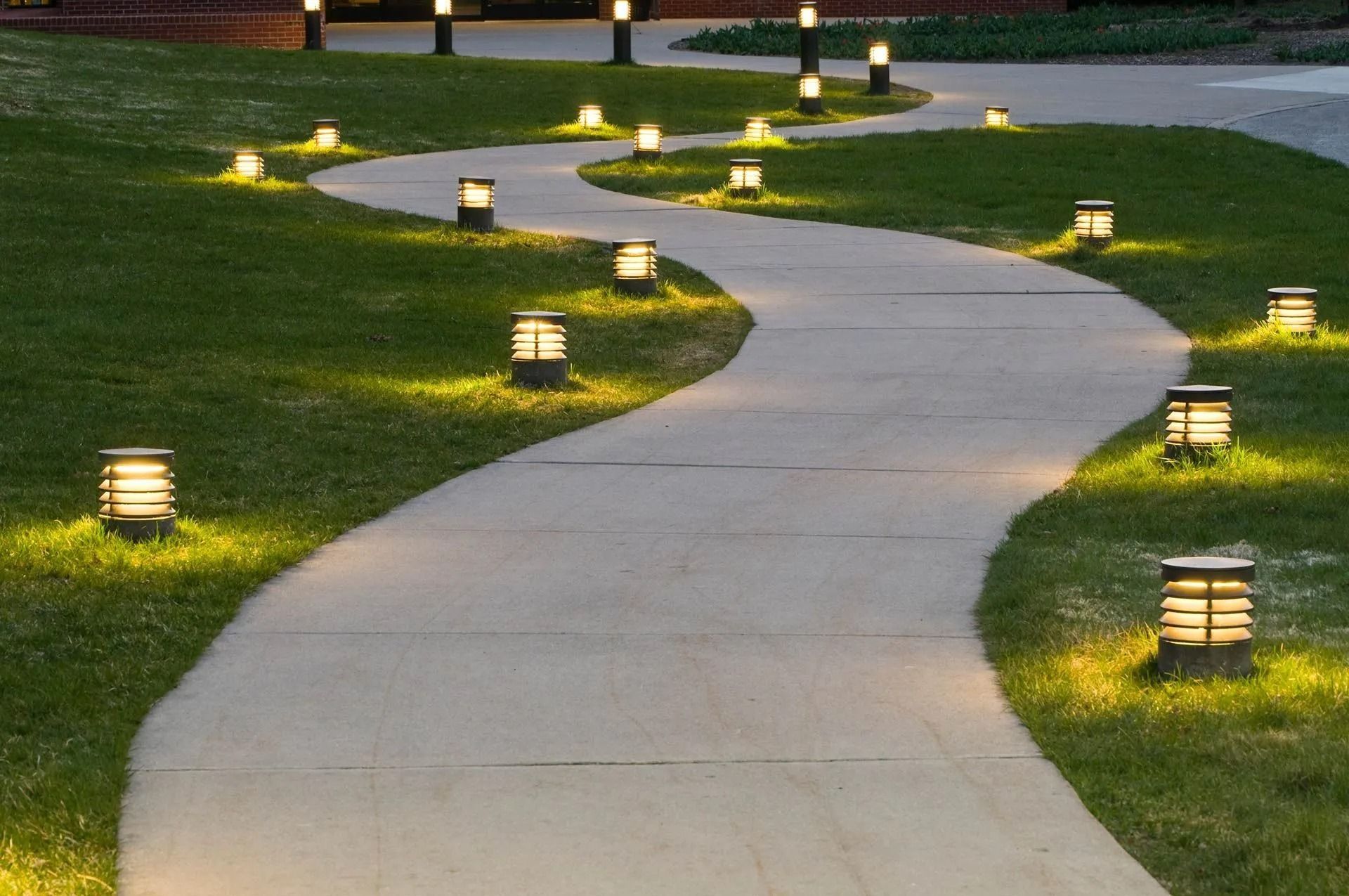 Pathway winding through green grass, lit by glowing outdoor lamps.