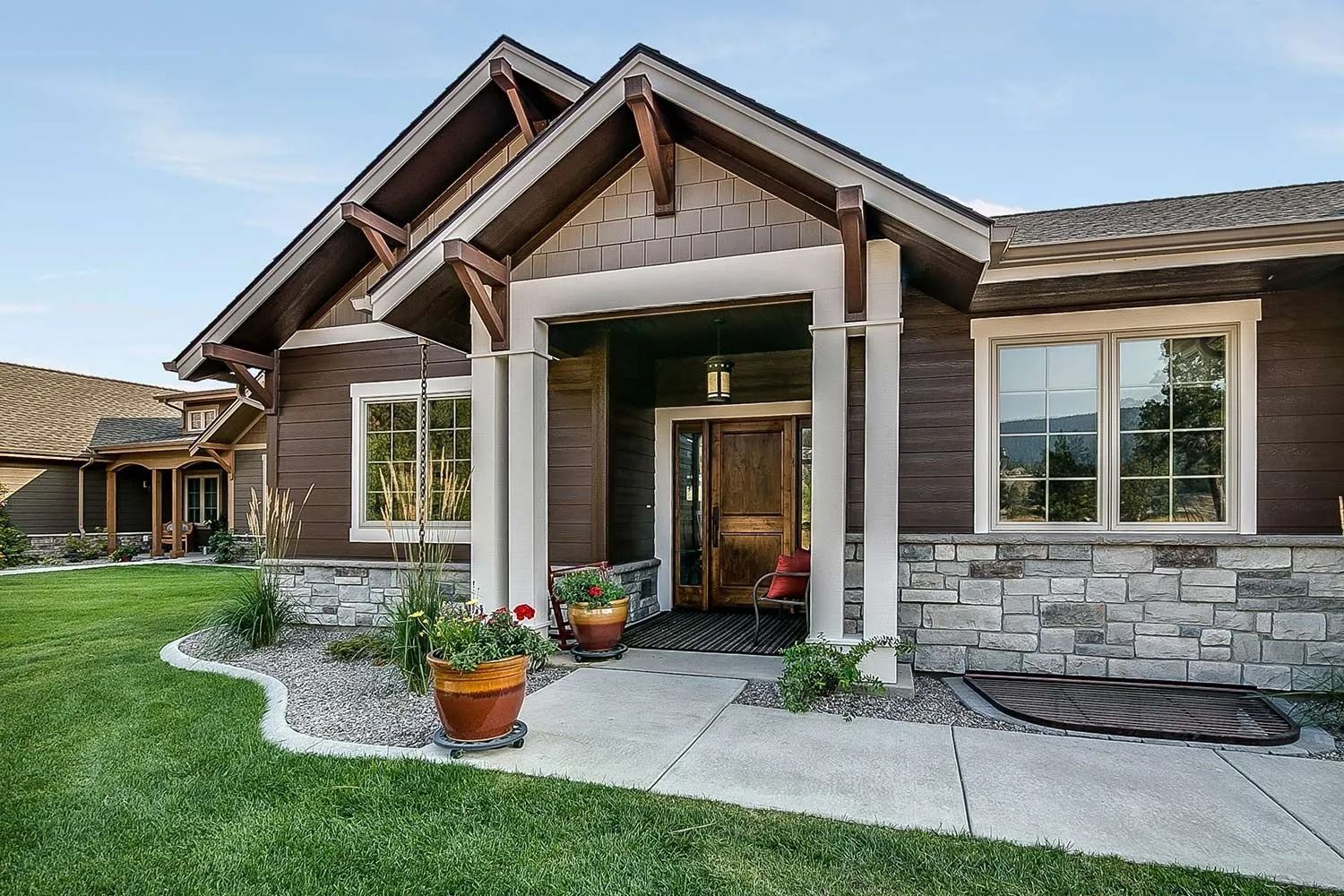Brown and gray home with stone accents, a covered entrance, and a well-manicured lawn.