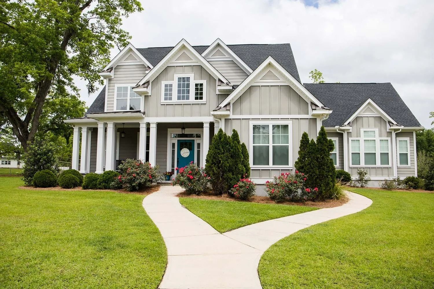 A gray two-story house with a blue door, white trim, and a split walkway through a green lawn.