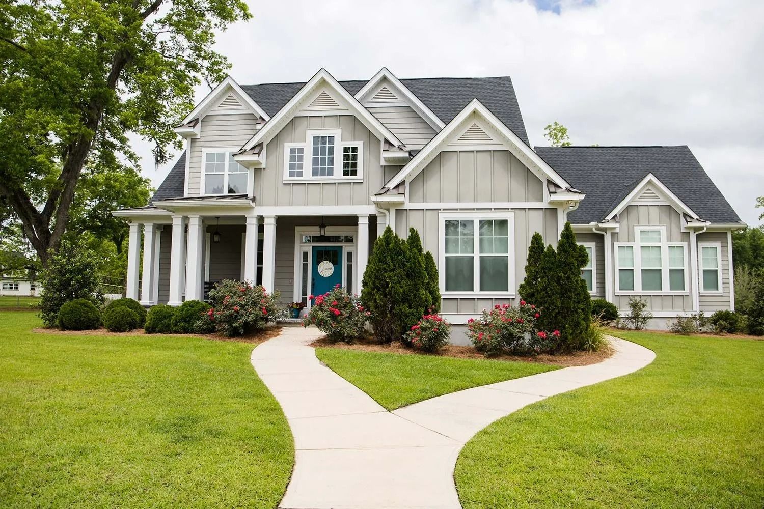 Gray house with a dark roof, white trim, and a blue front door; a curved walkway leads to the entrance.