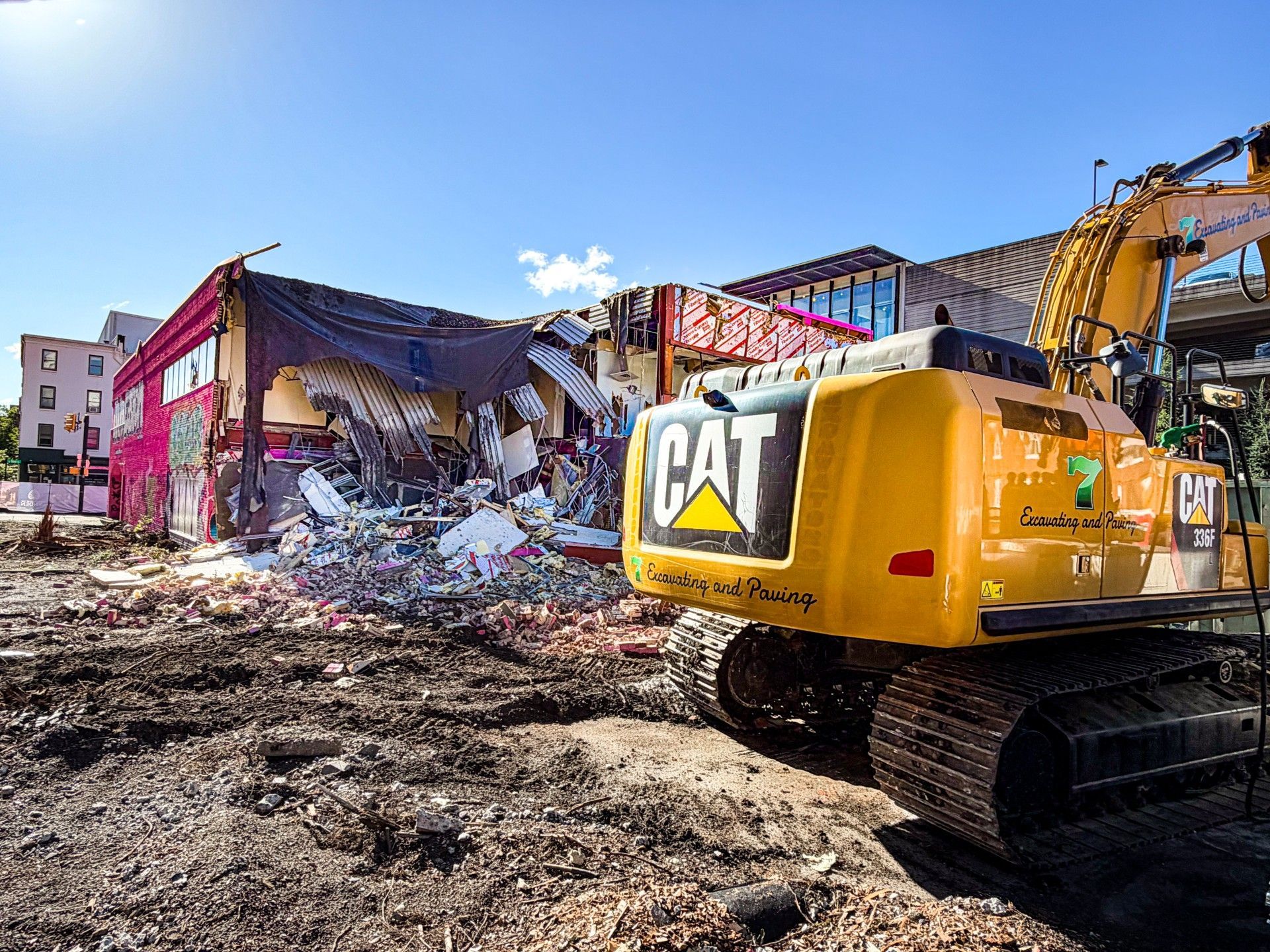 Yellow CAT excavator demolishing a damaged building under a clear blue sky