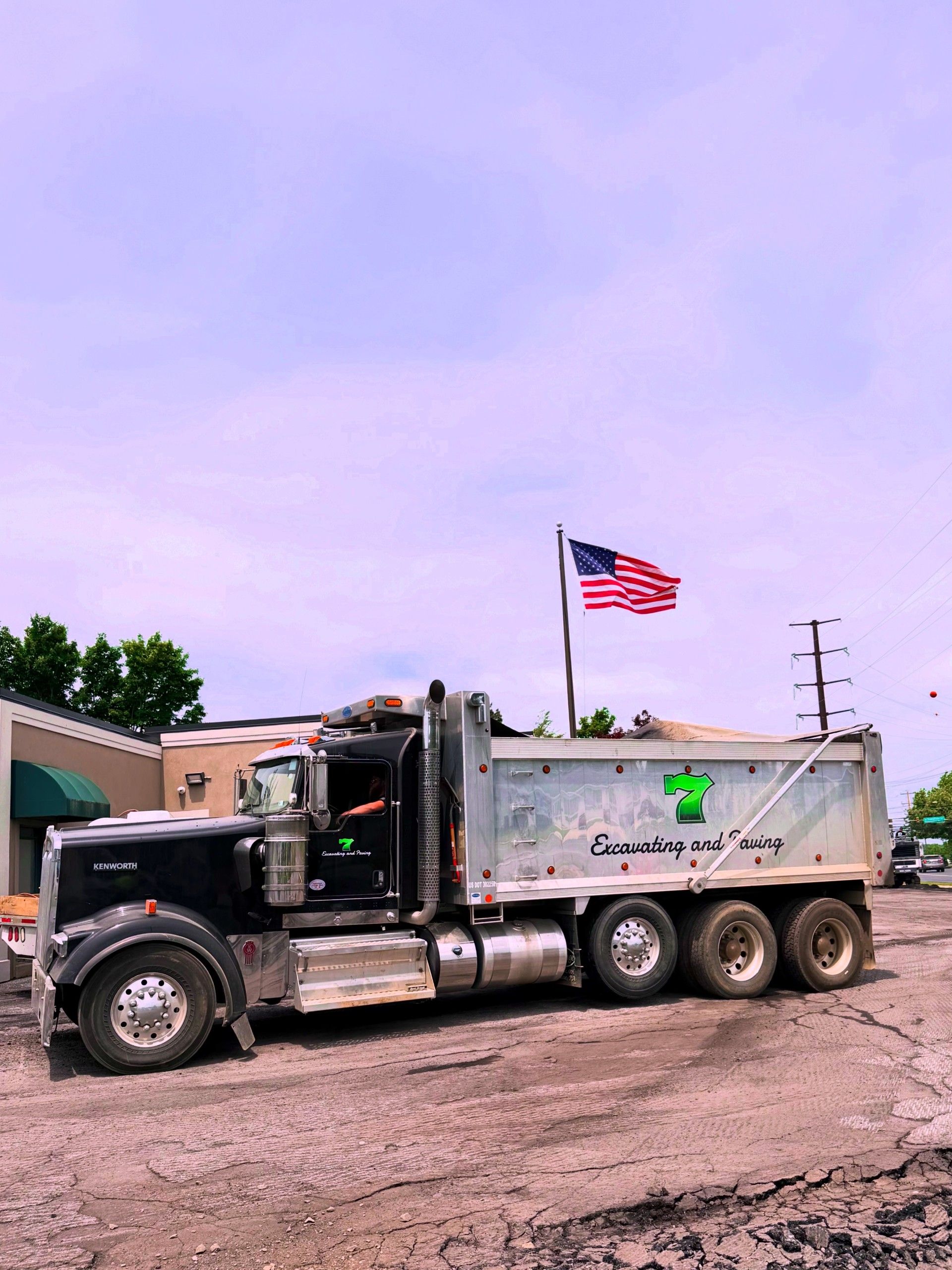 Black dump truck with American flag parked on a dirt lot under a cloudy sky
