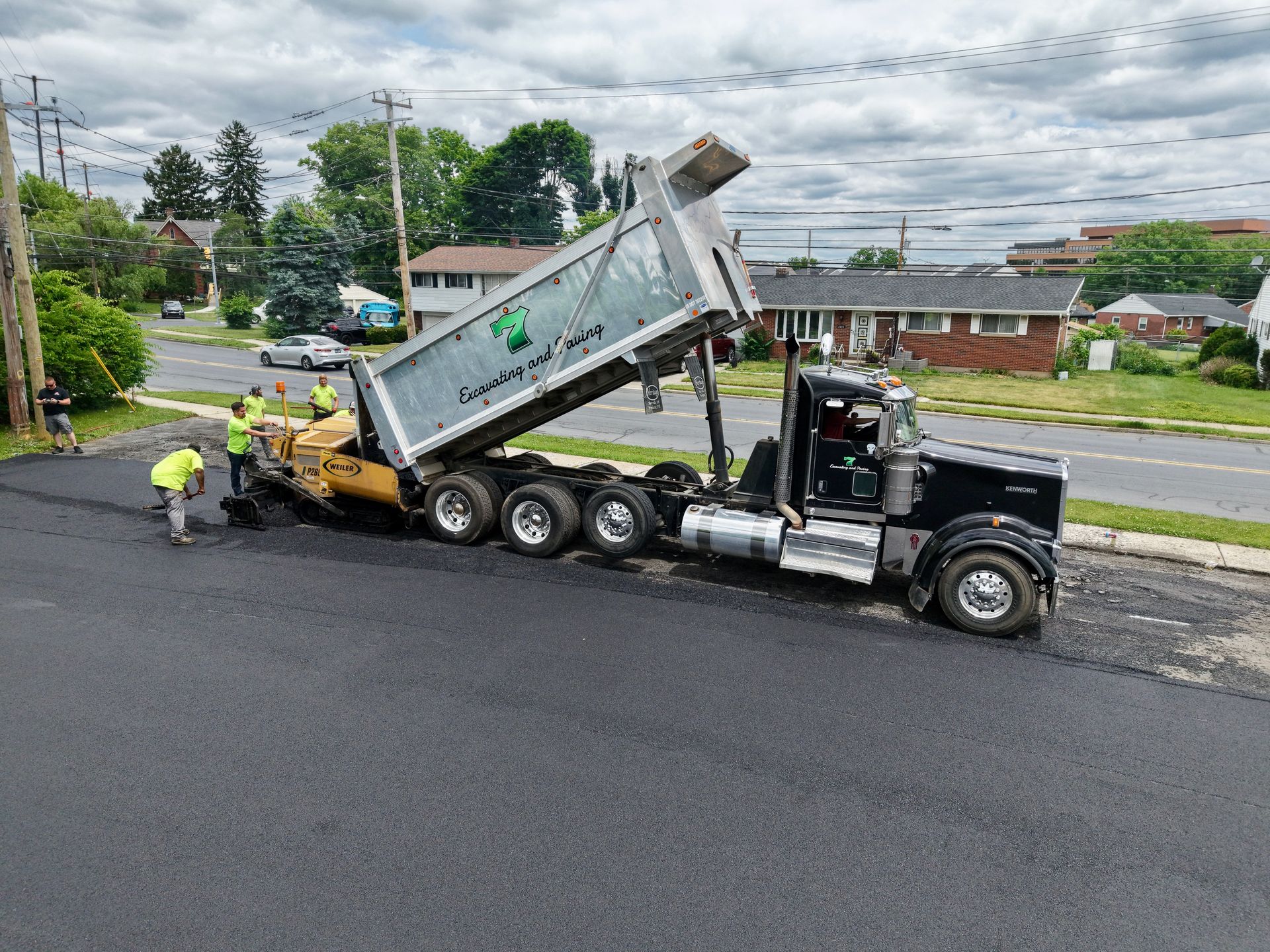 Dump truck unloading asphalt while workers pave a residential street