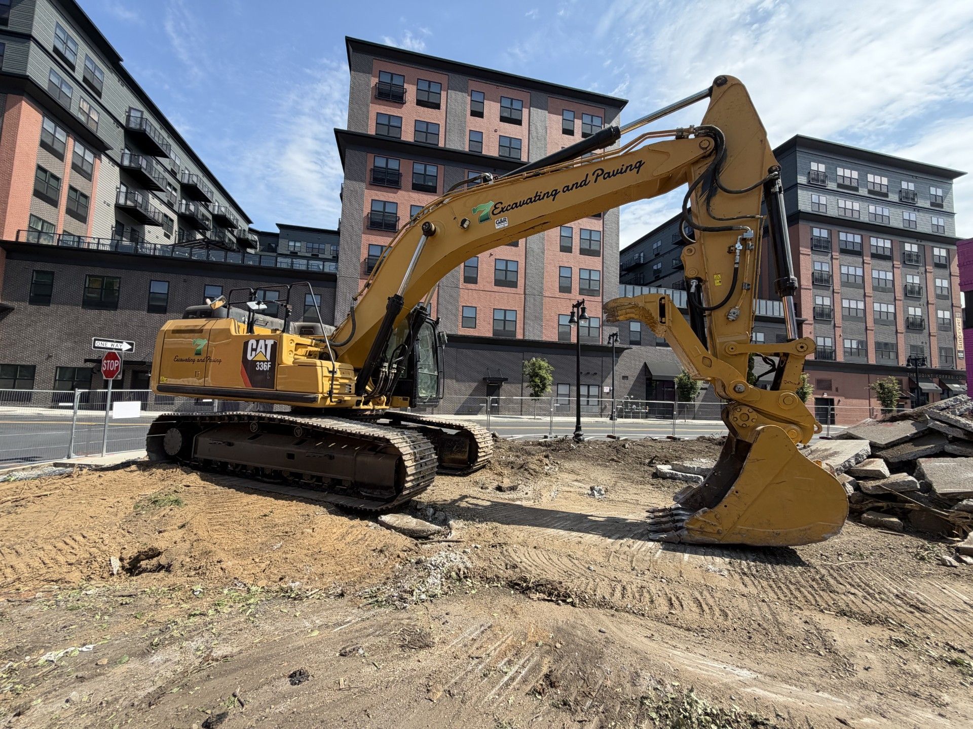 Yellow excavator at a construction site amid dirt and apartment buildings