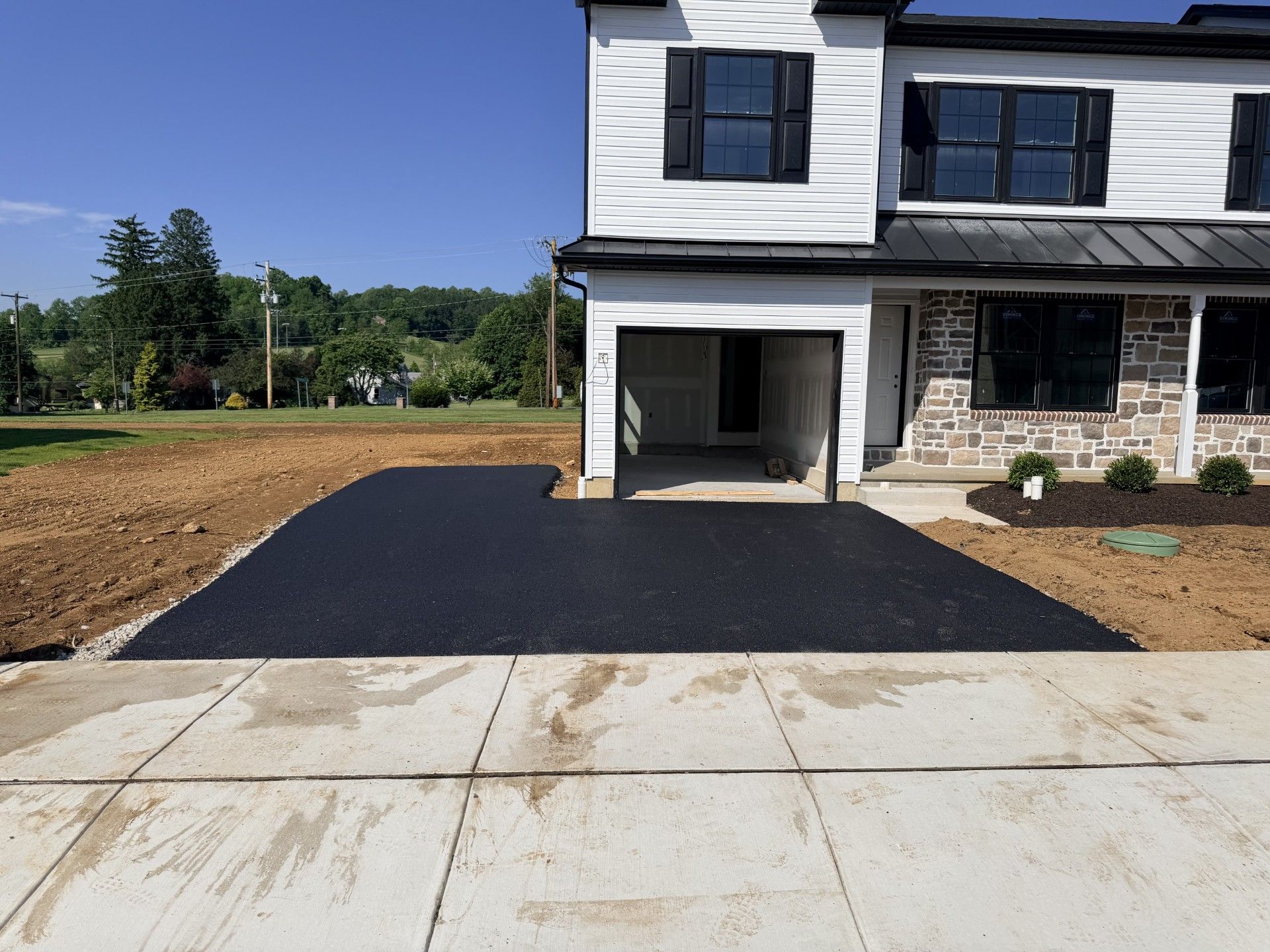 New house with black driveway apron and unfinished front yard beside a concrete driveway