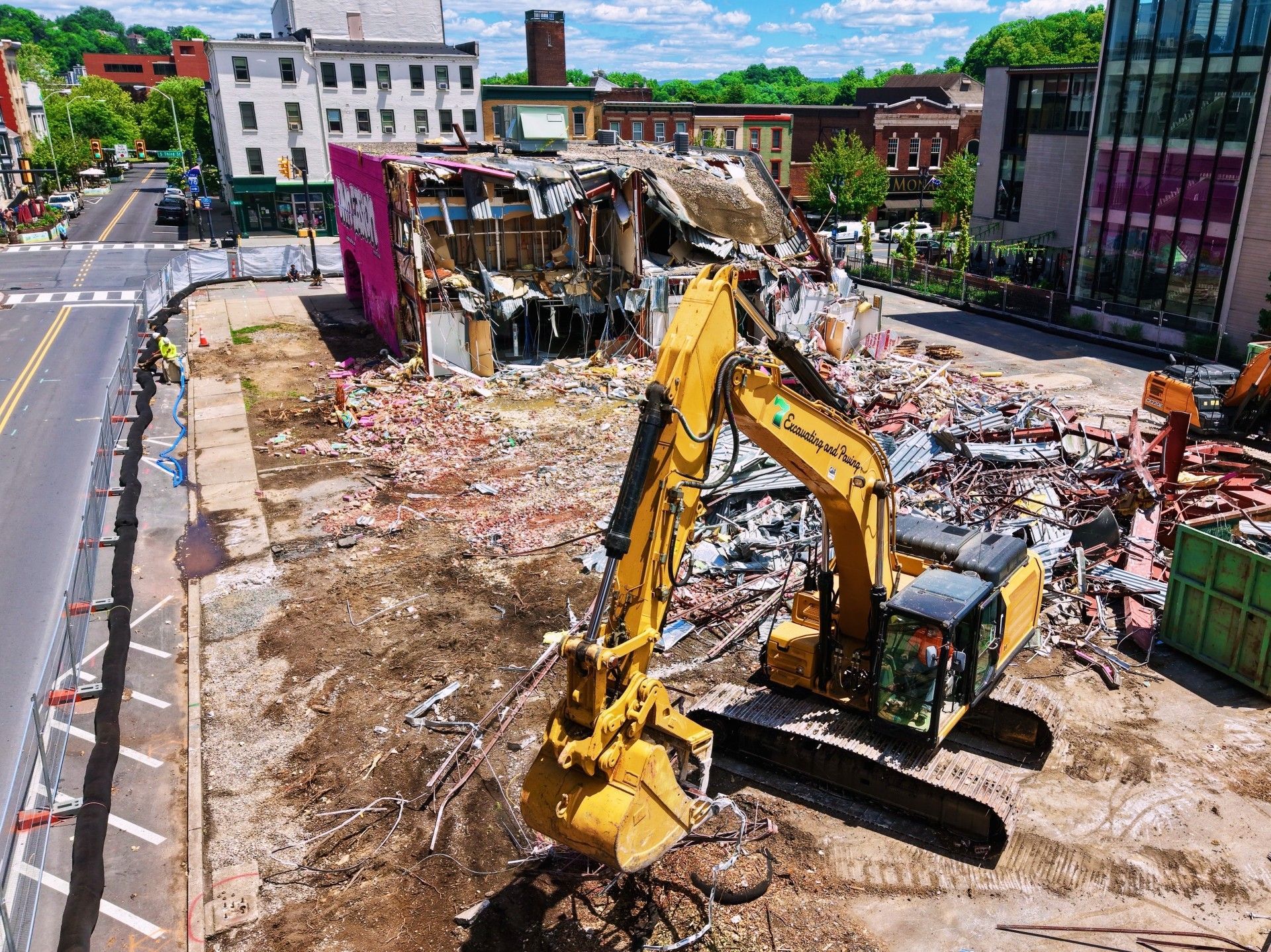 Yellow excavator demolishing a rubble-strewn building site beside a city street