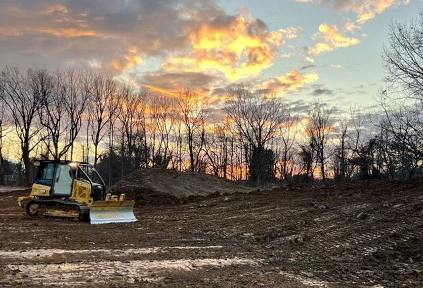 A bulldozer is driving through a dirt field at sunset.