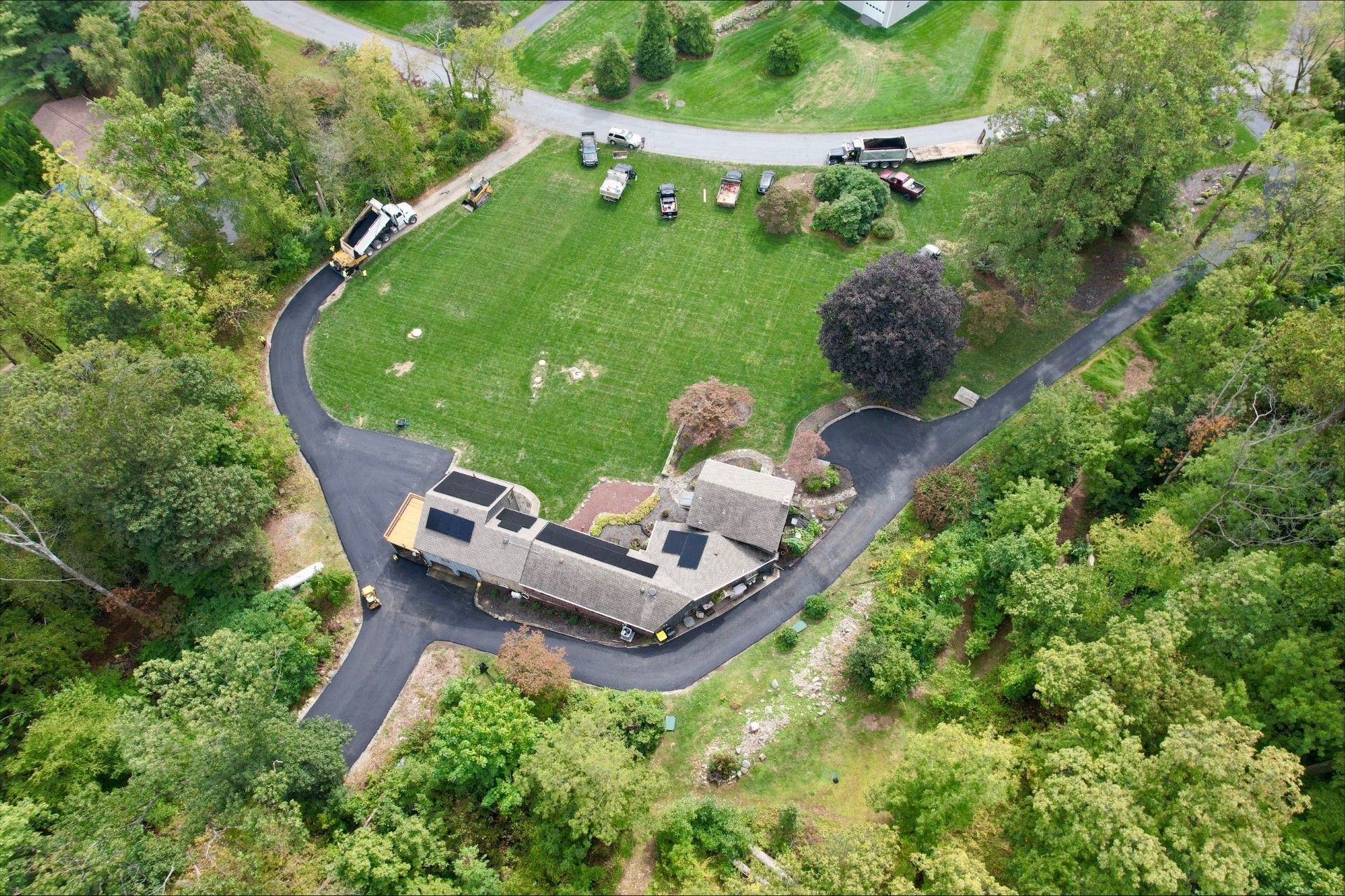 Aerial view of a house with a long, curving driveway, surrounded by trees and green grass.