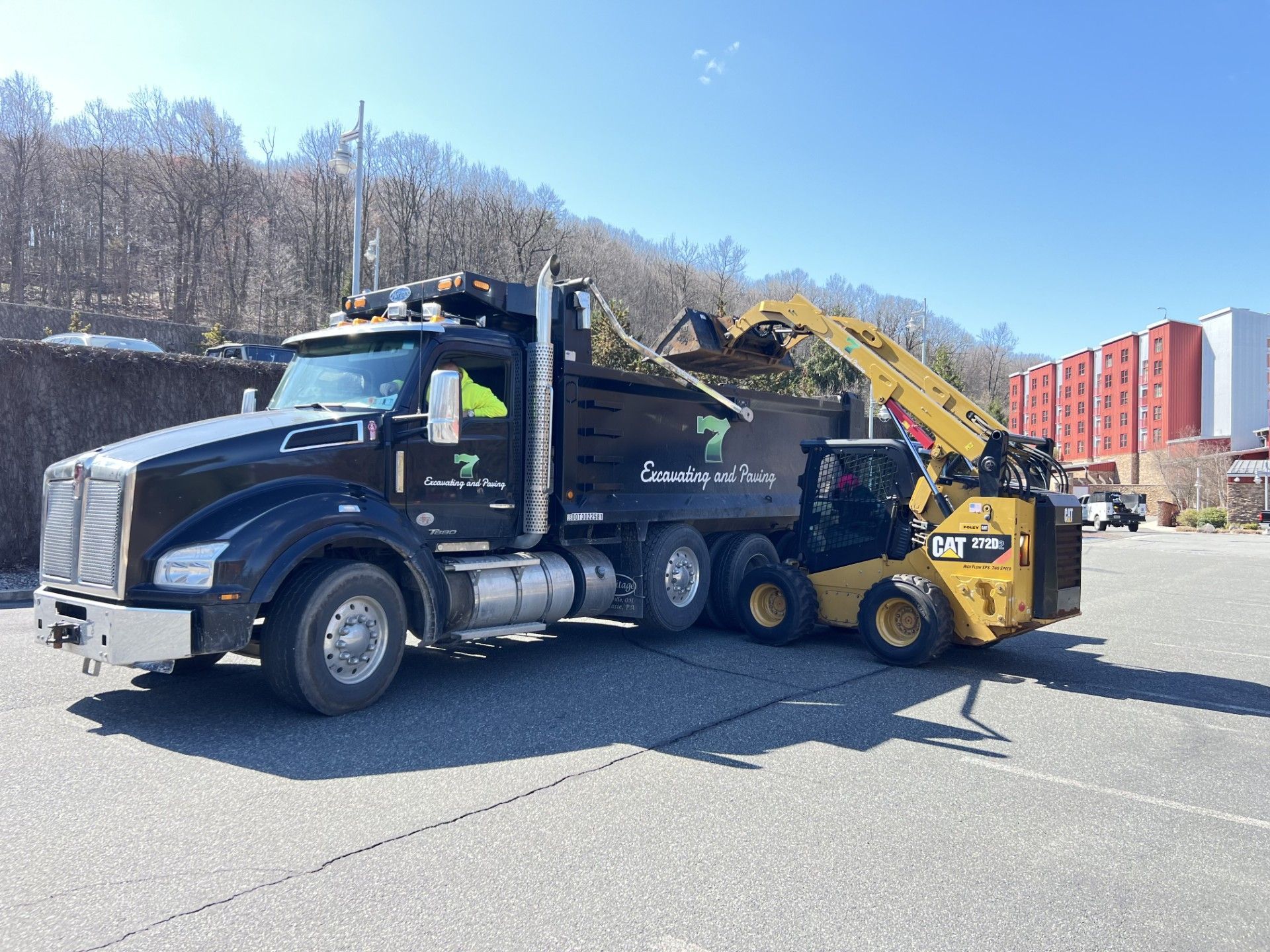 Black dump truck with a yellow front loader in a parking lot on a sunny day