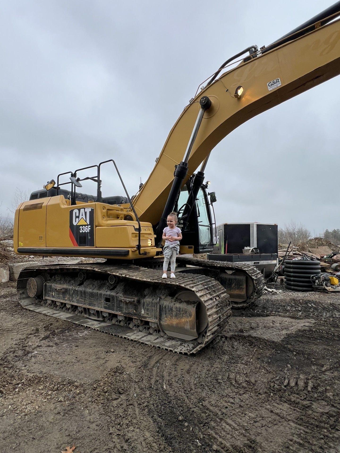 Yellow CAT excavator on muddy construction site with a person standing on the track.