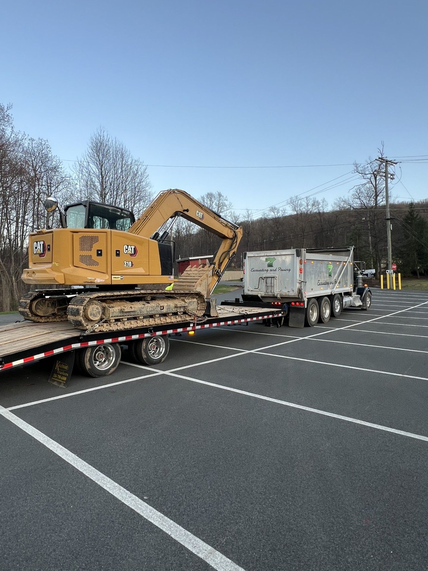 Yellow excavator on a flatbed trailer in an empty parking lot under a clear sky.