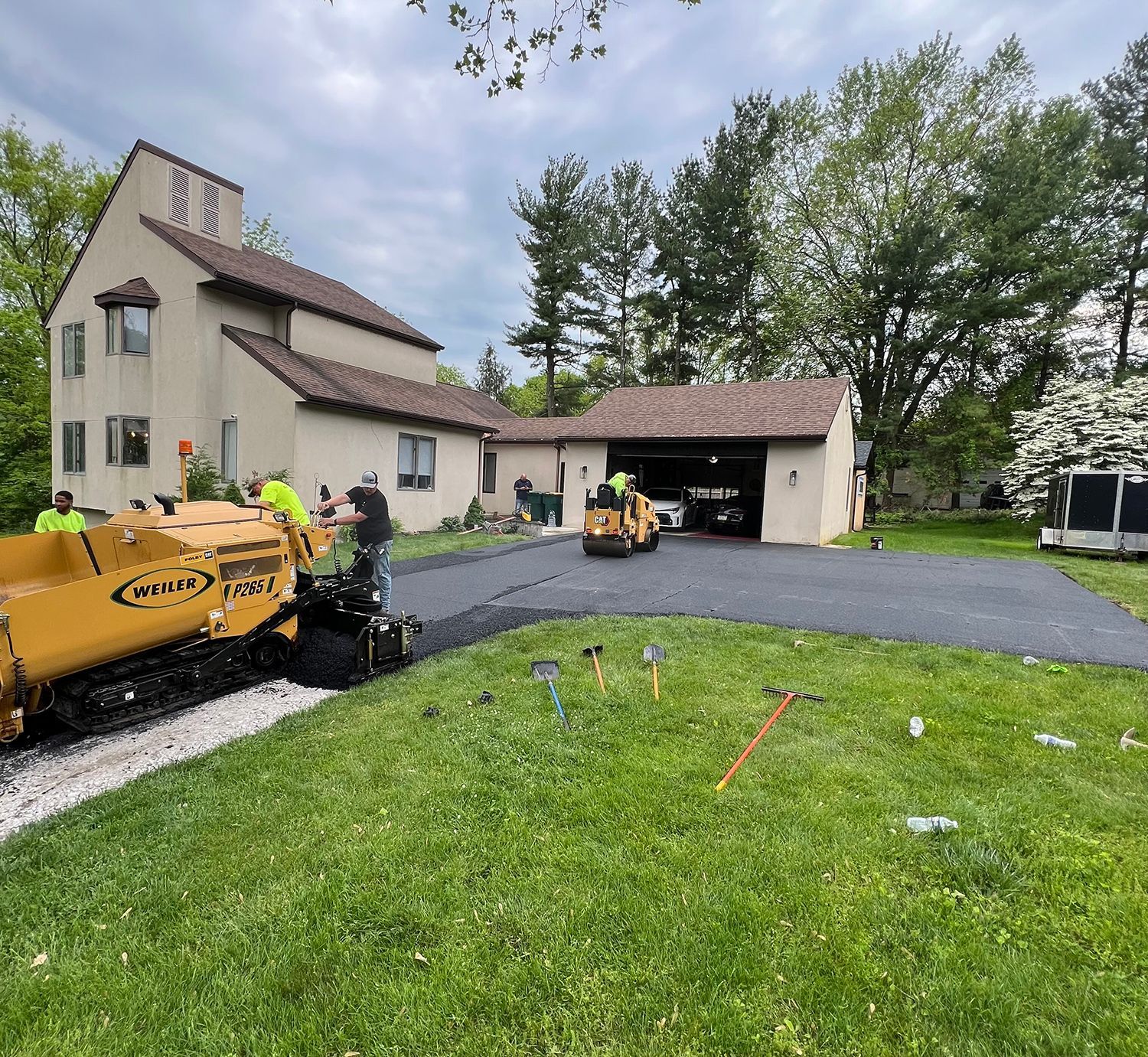 A group of people are working on a driveway in front of a house.
