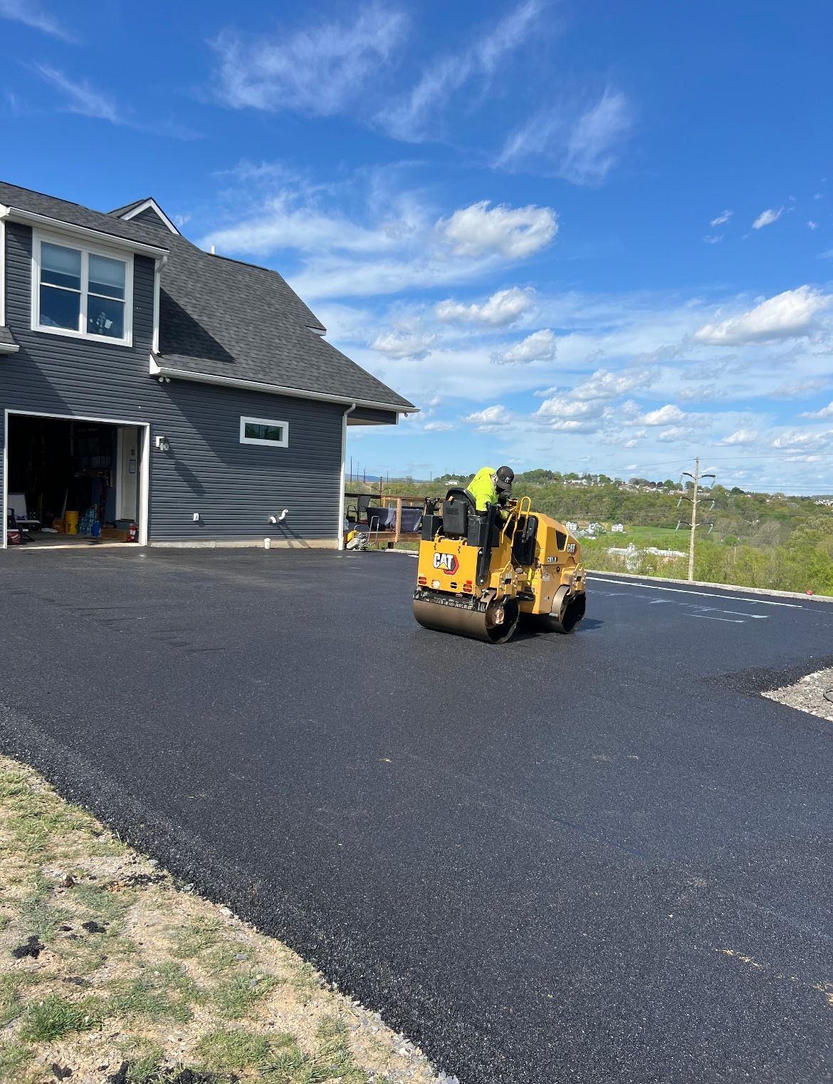 A roller is rolling asphalt in a driveway in front of a house.