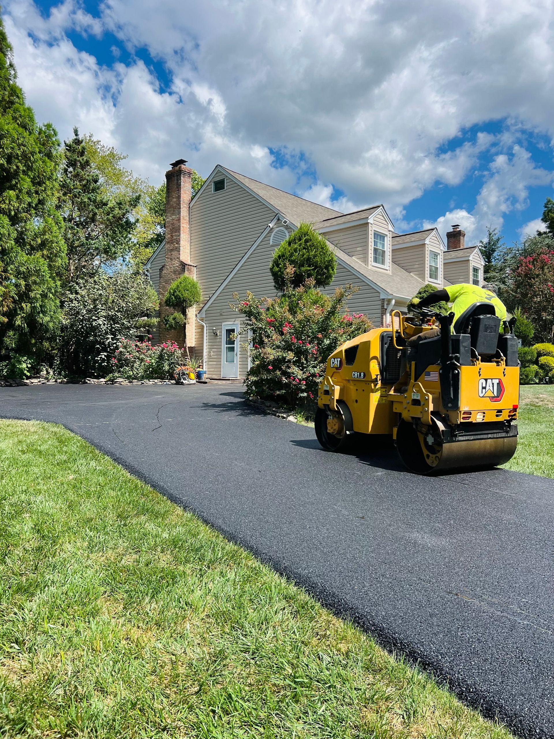 A yellow roller is stopped on a road in front of a house.