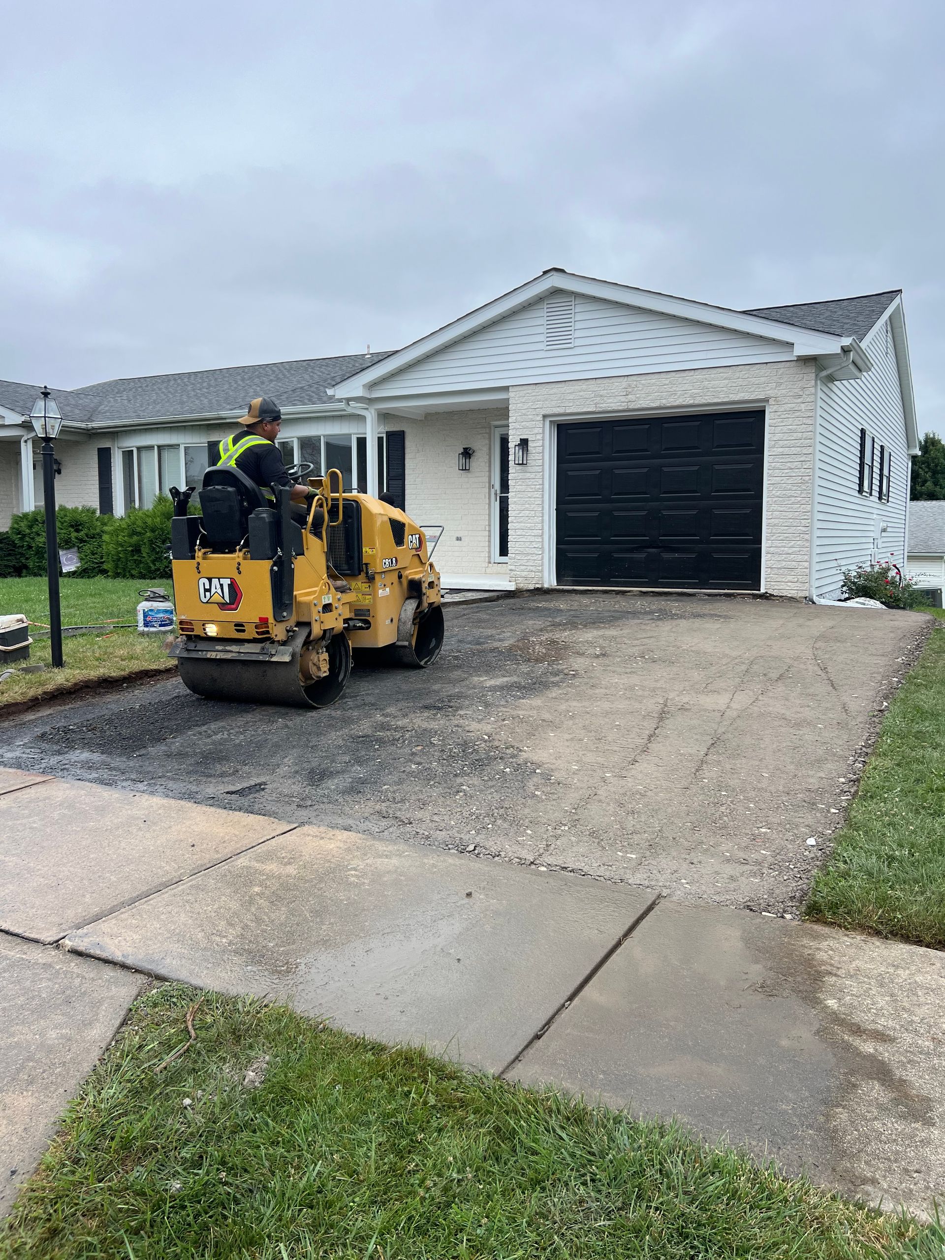 A man is driving a yellow roller on a driveway in front of a house.